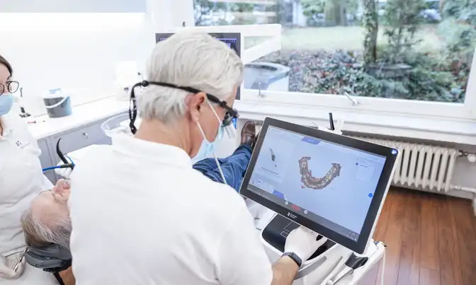 Dr. Tom Froböse schaut während einer Zahnbehandlung auf einen Monitor